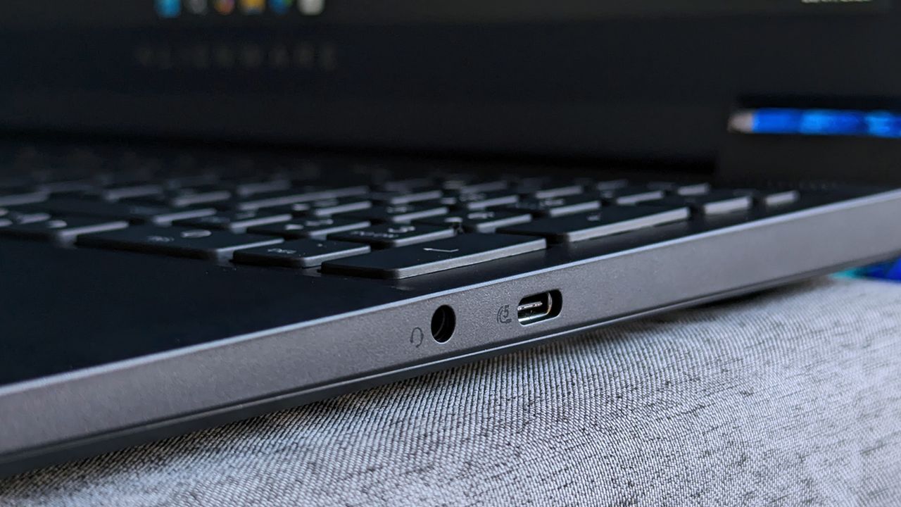 A close-up of an Alienware 15 laptop&rsquo;s right side shows a 3.5mm headphone jack and a USB‑C port, with part of the keyboard and faint Alienware branding visible on the bezel.