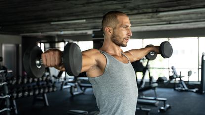 Young handsome man doing exercises in gym shoulder workout with dumbbell fitness health club