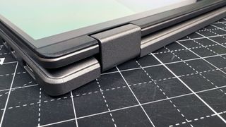 A close-up of the 360-degree hinges on the Asus Vivobook 16 Flip convertible laptop, resting on a black and white desk.