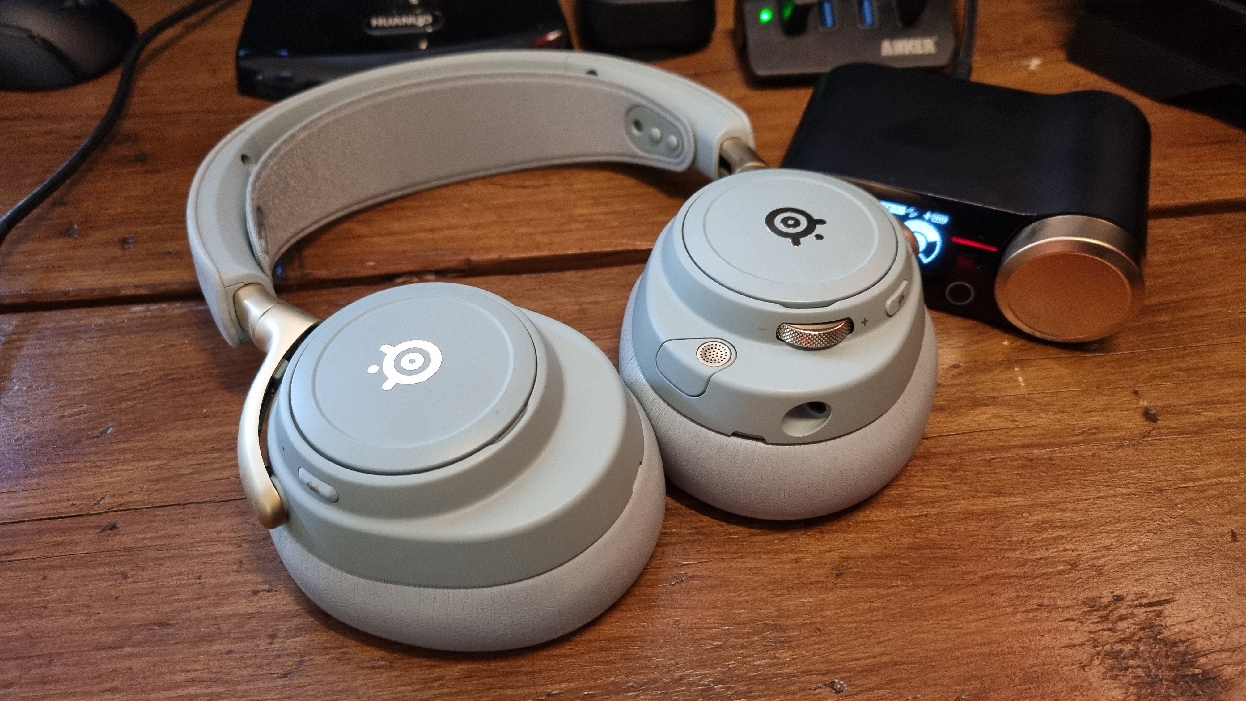 The SteelSeries Arctis Nova Elite gaming headset on a wooden desk, in "sage gold"