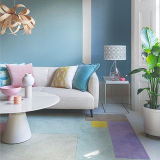 A pastel living room painted in two colours of blue with a colour-blocked rug and cream sofa with a round coffee table