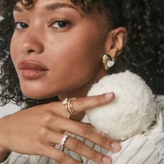 A woman wearing gold rings and statement earrings from Kendra Scott.
