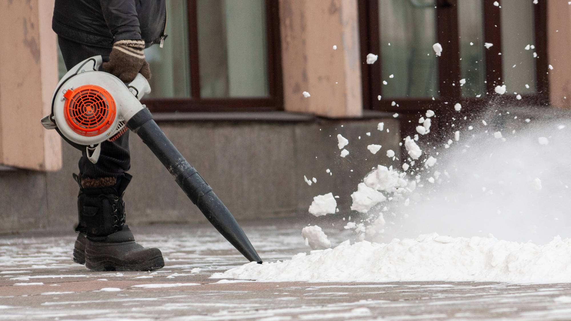 Man using leaf blower to blow snow off a sidewalk