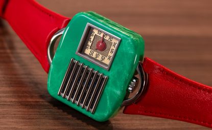 Futuristic watch, with green rectangular face, metal grille, and red strap