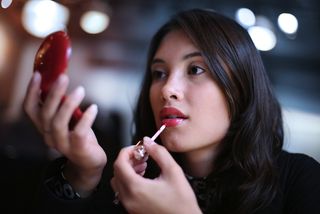 A woman applies lipstick with a small mirror.