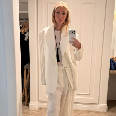 Gwyneth Paltrow takes a mirror selfie wearing a white oversized suit with white pointed-toe heels.