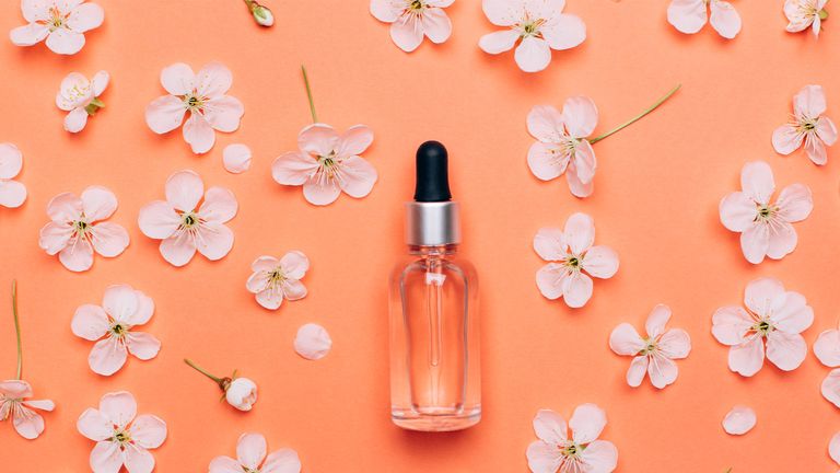 Natural cosmetics oil on a coral flower background. Spring care concept. Flat lay style.