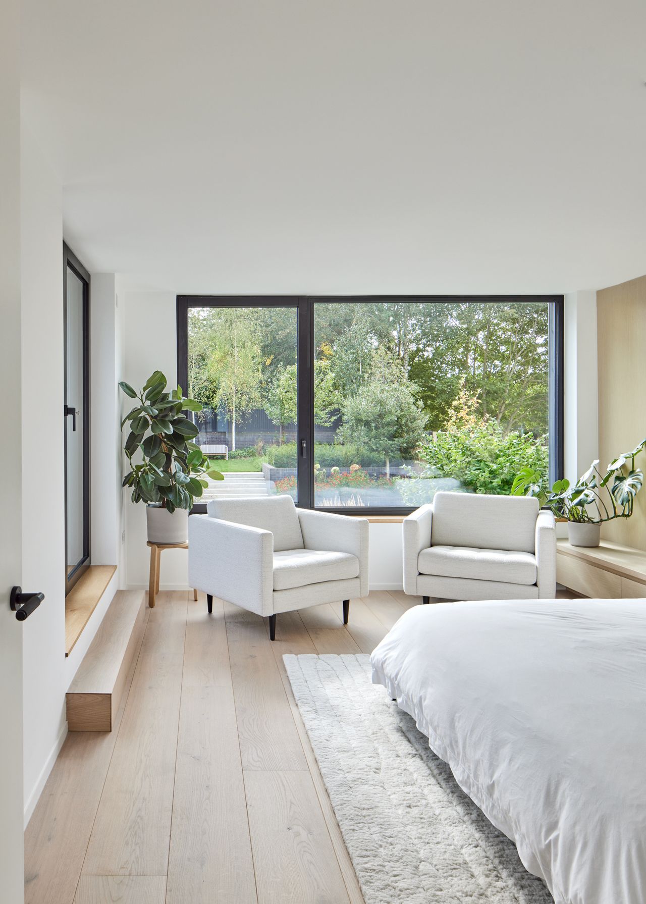 A contemporary bedroom with white armchairs and large glazed doors leading out to a garden