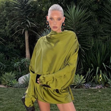 Elsa Hosk wears a green satin dress with a black woven bag and black mesh heels.
