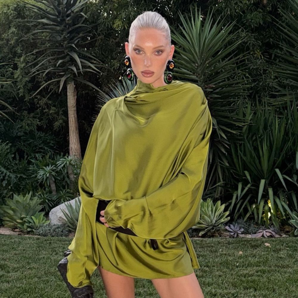 Elsa Hosk wears a green satin dress with a black woven bag and black mesh heels.