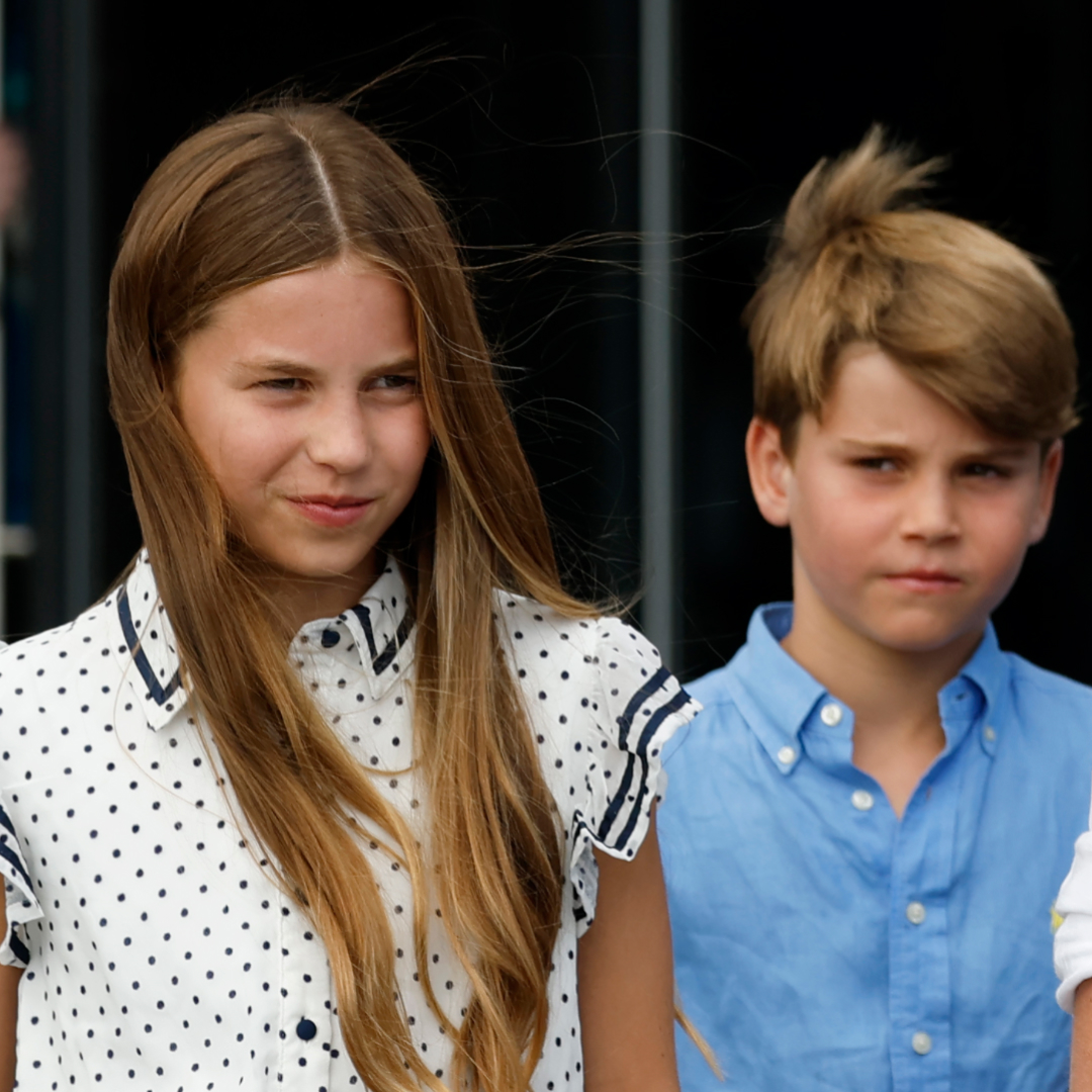 Princess Charlotte has long dark blonde hair and wears a white and black polka dot dress while Princess Louis wears a blue shirt