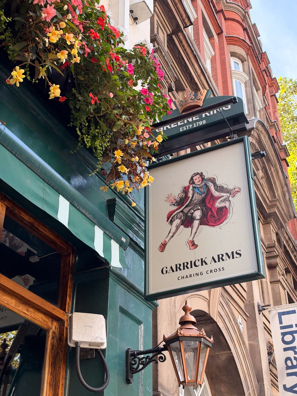 Carrick Arms pub sign at Charing Cross surrounded by colorful hanging flowers and historic brick buildings.