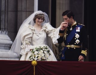 Princess Diana in her wedding dress holding a bouquet as Prince Charles kisses her hand on the Buckingham Palace balcony