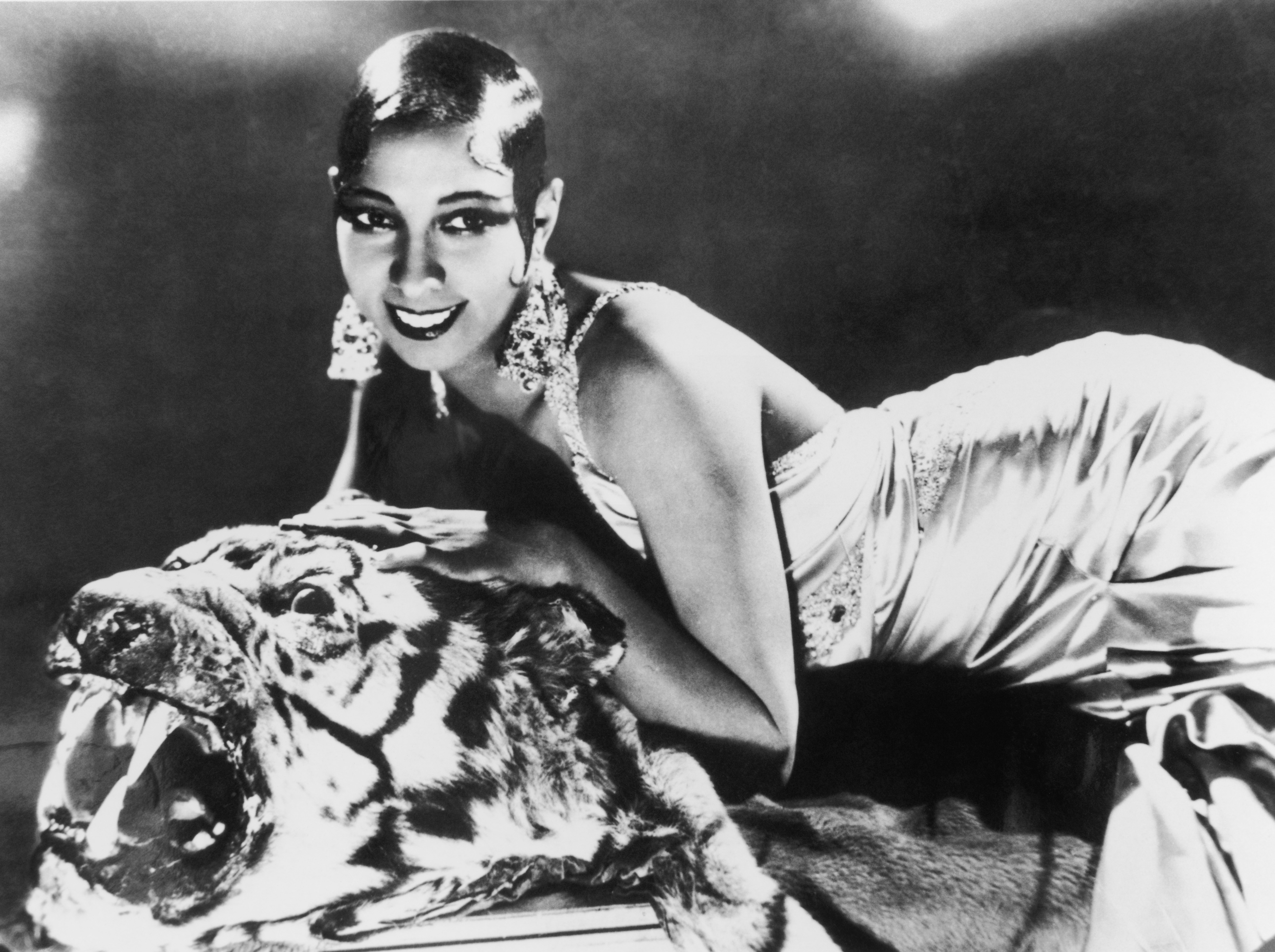 circa 1925: a Portrait of American-born singer and dancer Josephine Baker (1906 - 1975) lying on a tiger rug in a silk evening gown and diamond earrings.