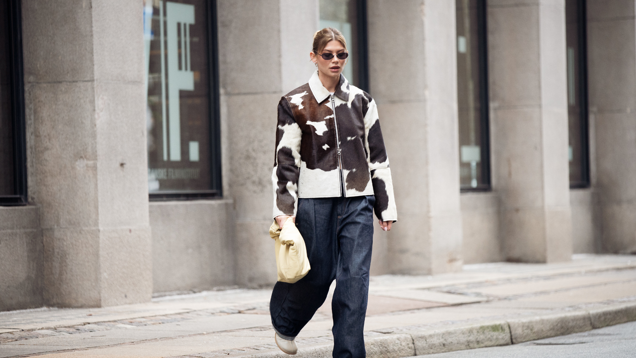 Sophia Geiss wears cow print cropped jacket with a zipper, pale yellow bag, blue wide jeans during the Copenhagen Fashion Week Autumn/Winter 2025