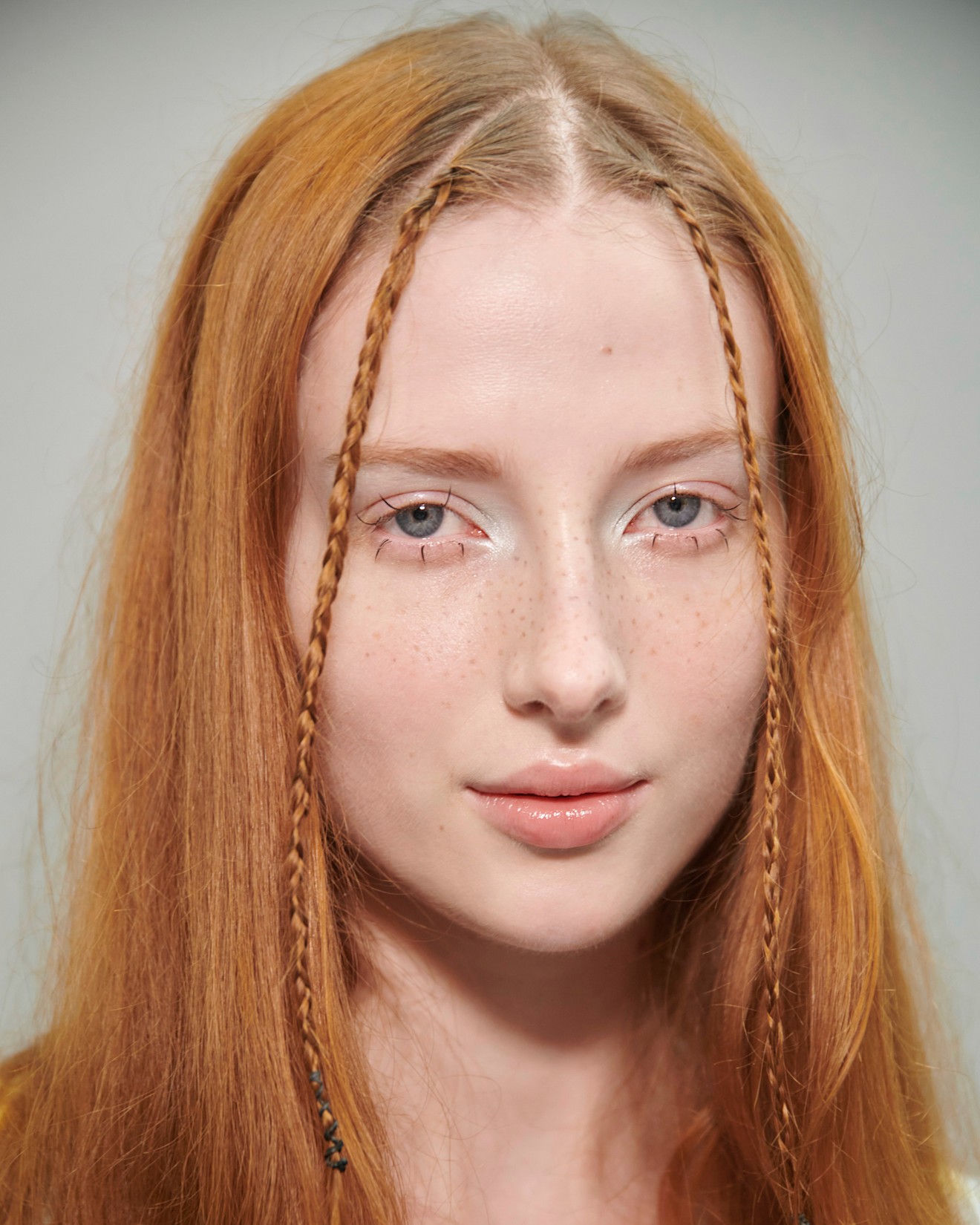 a model with red hair and two small braids in her front pieces poses for a portrait.