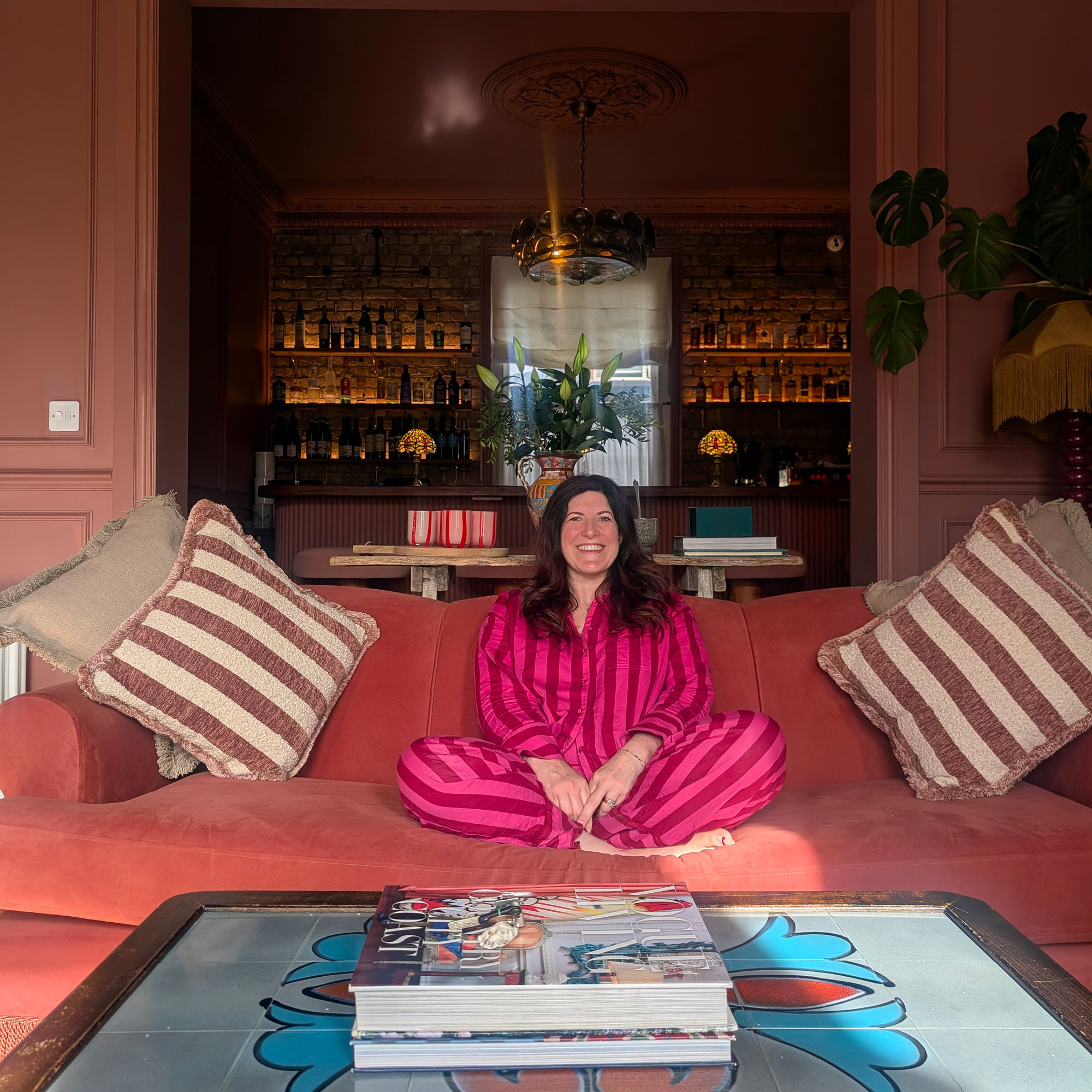 Woman in pink stripy pjs on coral sofa with striped cushion on either side
