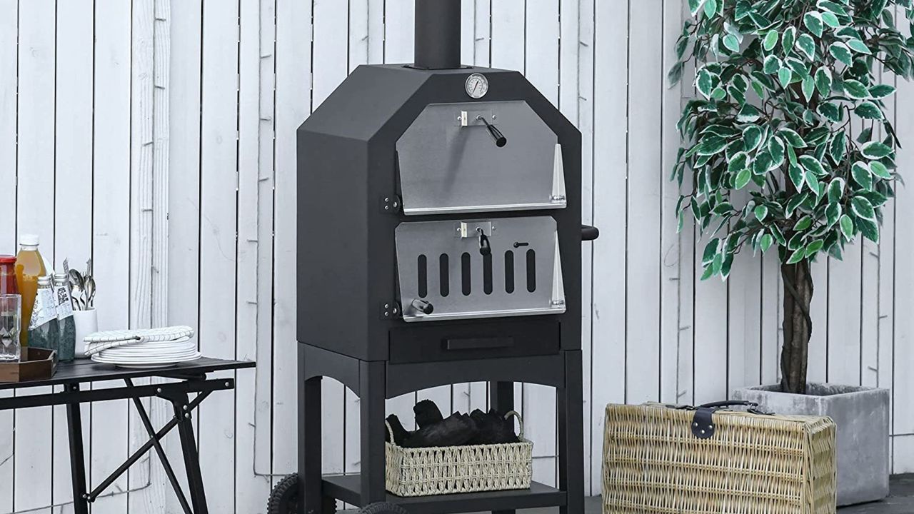 Outsunny Outdoor Charcoal Pizza Oven in garden in front of white fence