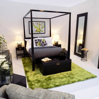 bedroom with white wall black frame bed with designed cushion mirror and white floor with green rug on
