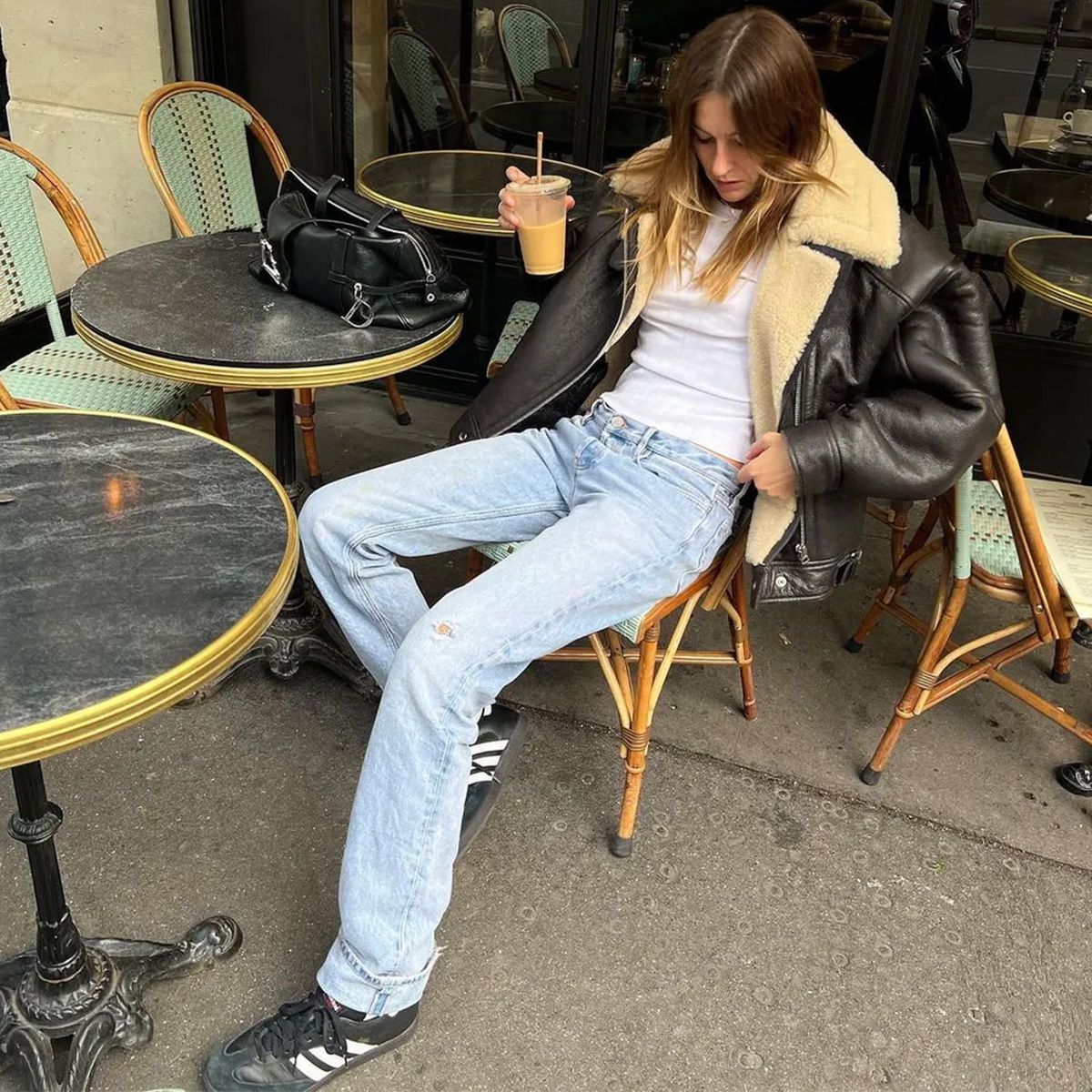 Camille wears a black coat with fur trim, white t-shirt, jeans, and adidas sambas.