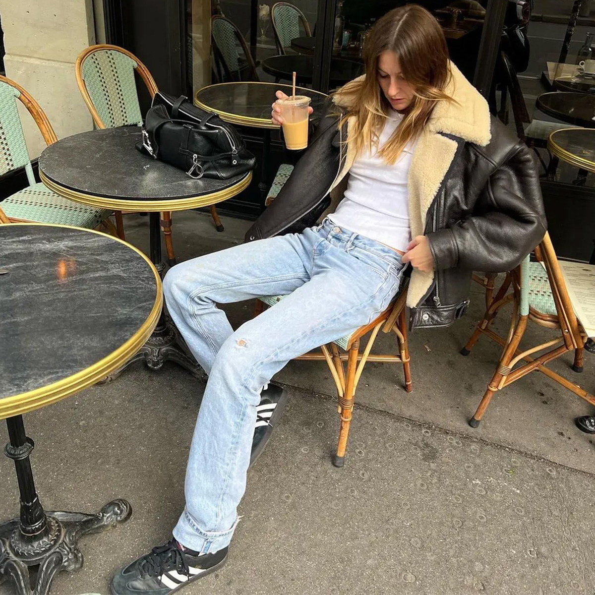 Camille wears a black coat with fur trim, white t-shirt, jeans, and adidas sambas.