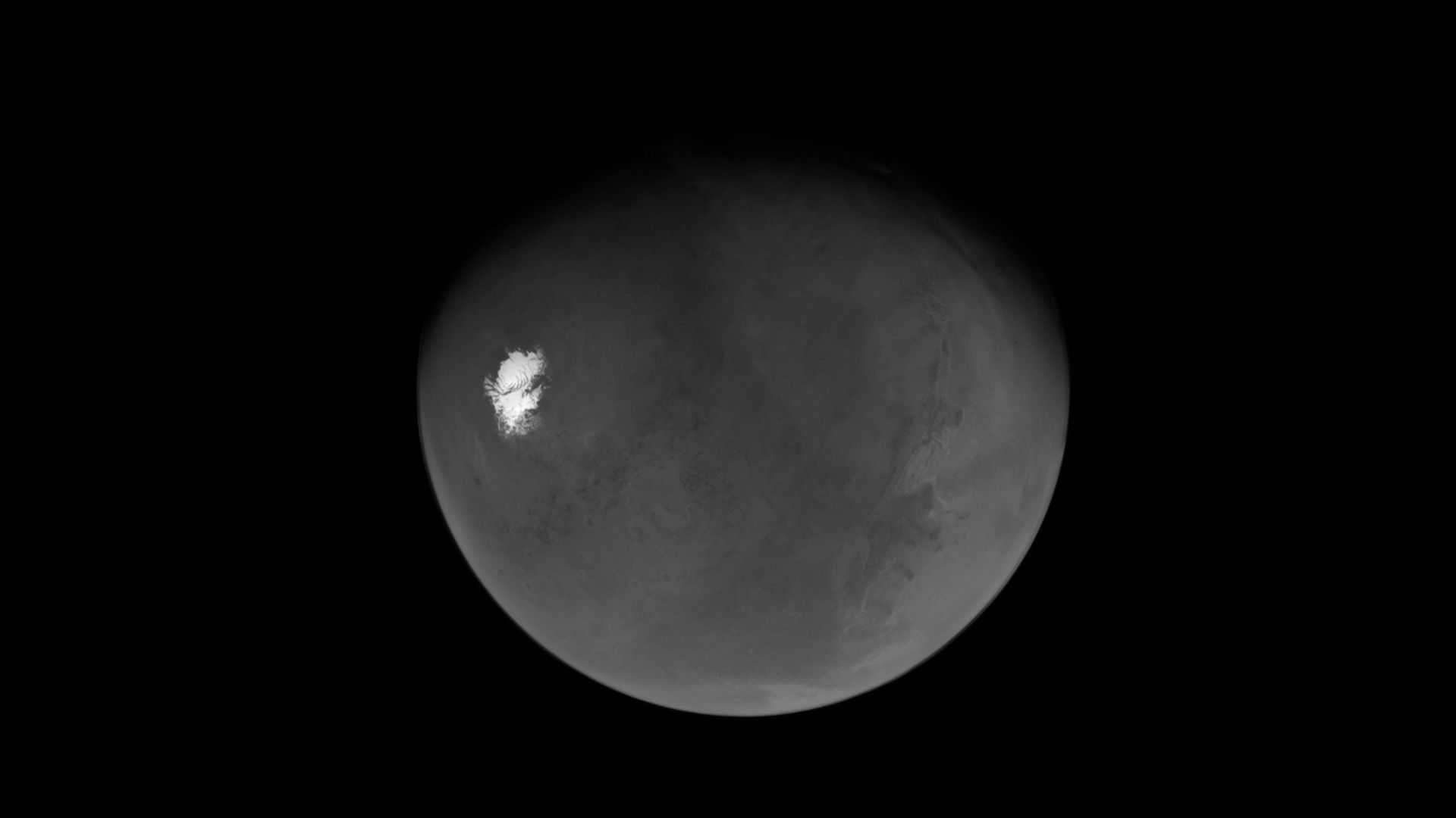 A black and white view of a planet. A white blob is on the left.