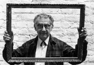 Painter, photographer and film-maker Man Ray (1890 - 1976) peering through a picture frame which he is holding up as he stands against a whitewashed wall. (Photo by Joseph McKeown/Express/Getty Images)