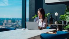 A financial adviser smiles as she works on her laptop in her office.