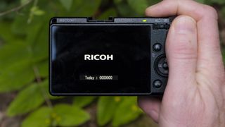 Ricoh GR IIIX camera in the hand with screen displaying a zero photo count for the day 