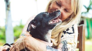 a woman smiles as she holds a small senior dog outside in a chair