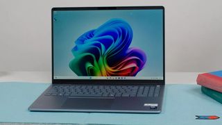 A sleek laptop with a vibrant blue and green abstract wallpaper on the screen, placed on a light blue surface next to colorful books.