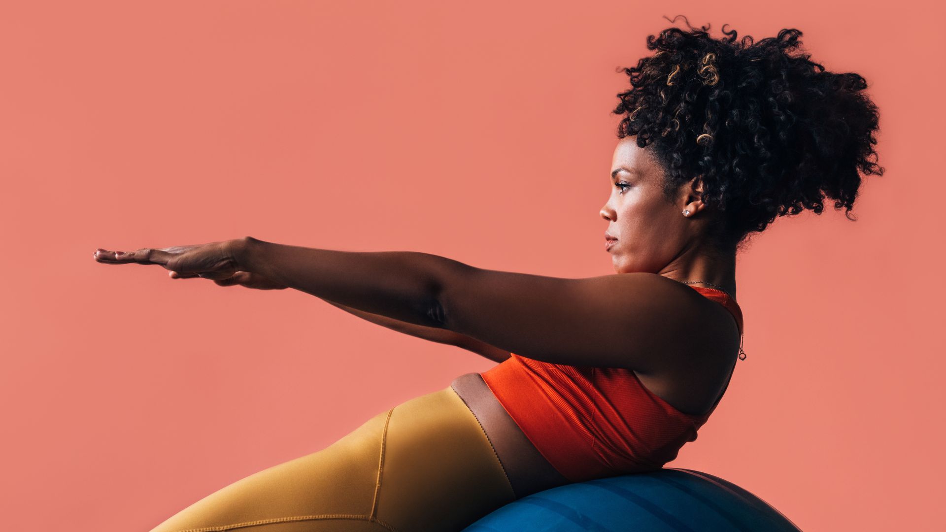 Woman doing gym ball exercises in activewear, hands stretched out for balance, concentrating face