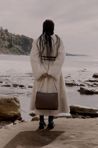 Woman facing the ocean with bag behind her back