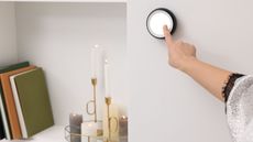 A Caucasian woman's hand adjusting a round hygrometer thermostat on a white wall, a shelf with lit candles and stacked books beside it