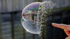 A man's finger bursts a large soap bubble.