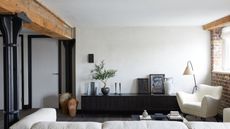 Industrial loft style living room with exposed beams and brick wall, plaster walls, console table with artwork and potted plant, boucle chair, white sofa and floor lamp