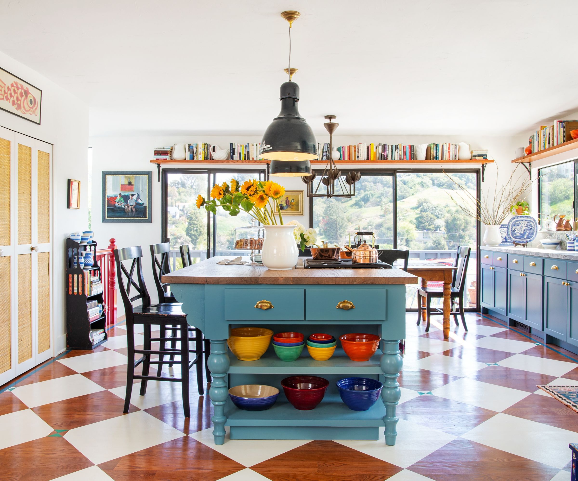 A colorful kitchen with white walls, blue cabinets, and wooden floors painted with a checkerboard pattern