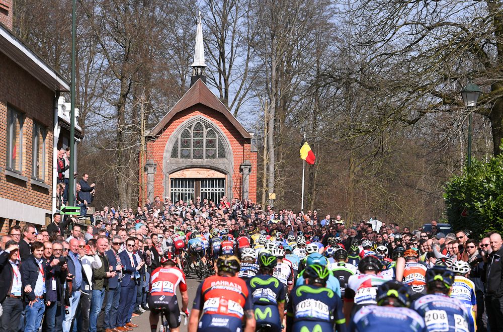 The peloton climbs toward a chapel and the Belgian flag during E3 Harelbeke