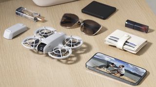 DJI Neo sobre una mesa de pino con el teléfono y otros elementos esenciales que muestran el tamaño compacto del dron