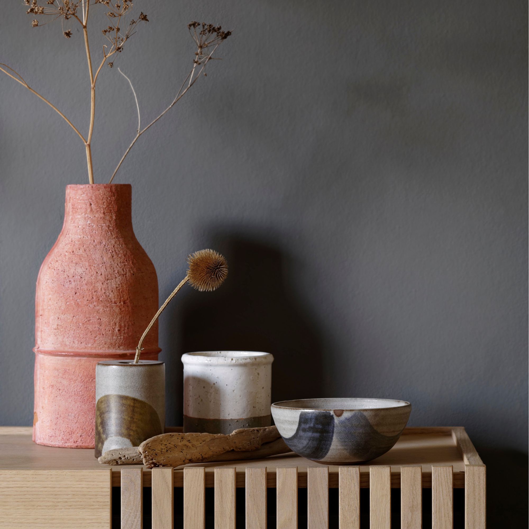 Two stem vases on top of a wooden unit in front of a grey wall