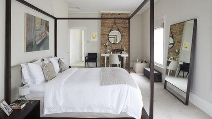 A small bedroom with four poster bed and exposed brick wall
