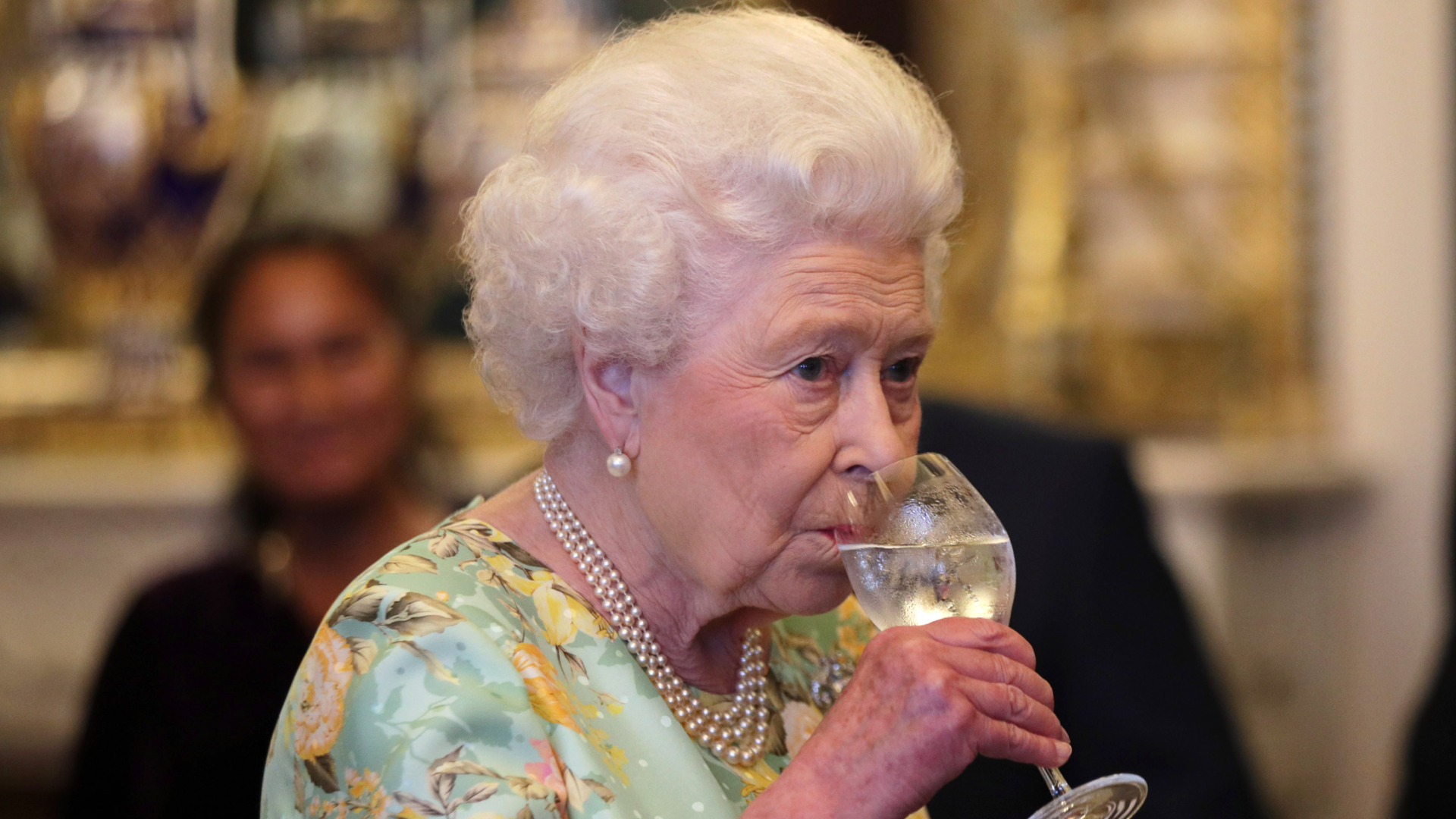 Queen Elizabeth wearing a green floral dress drinking a glass of water