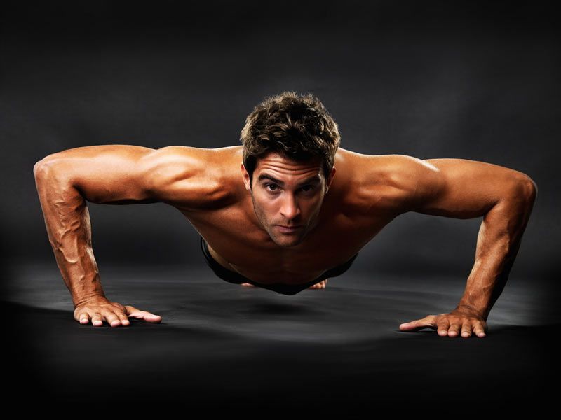 Full length of muscular guy doing pushups on black background 