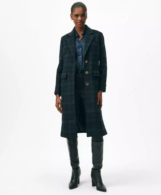 A black female model wearing a blue and green plaid wool coat and tall black boots