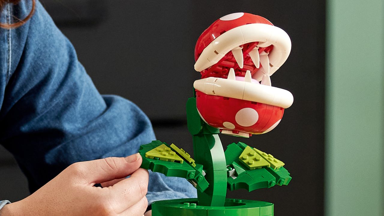 An open-mouthed Lego Piranha Plant, with its leaf being held by a hand