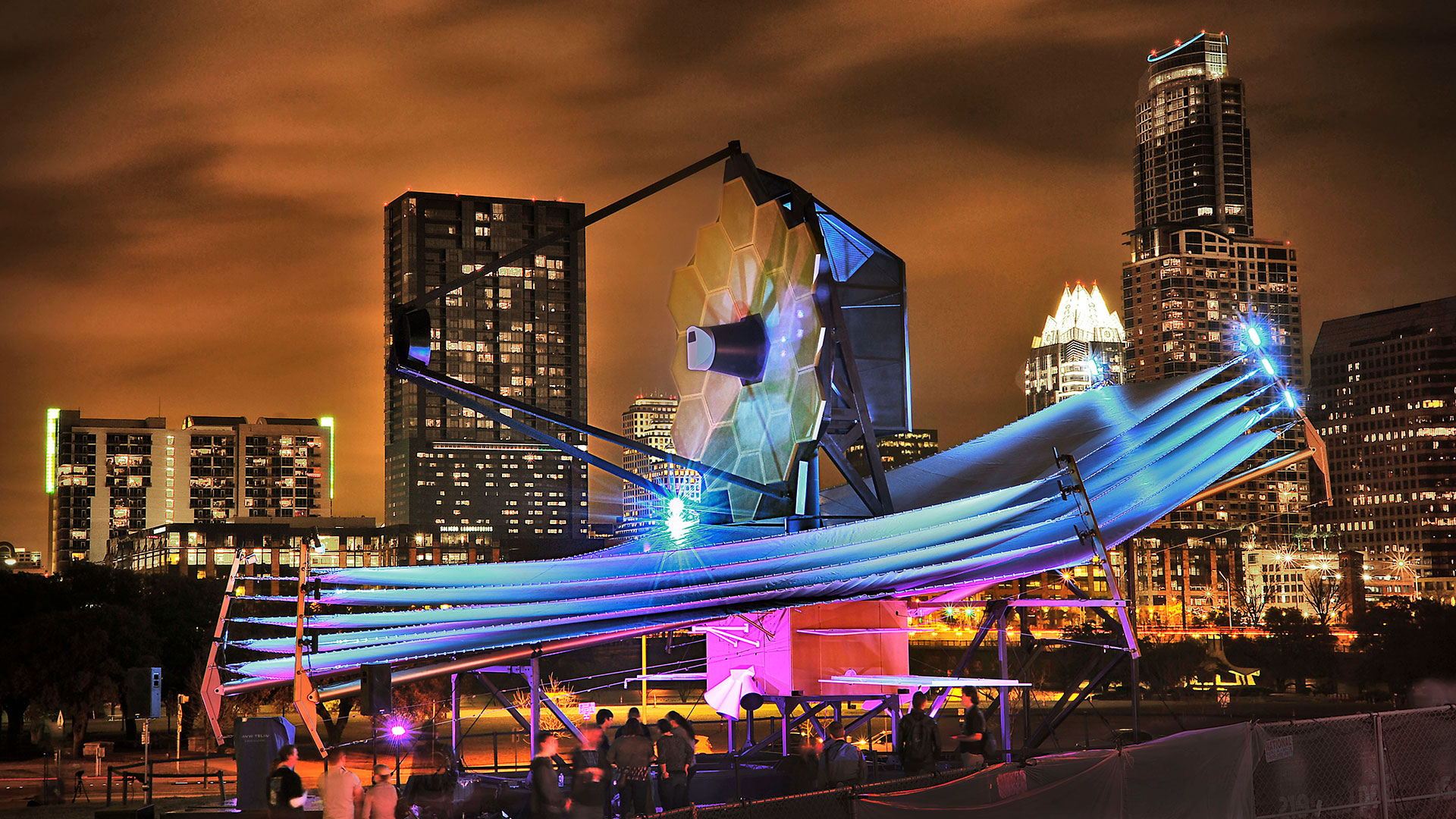 a full-size model of the james webb space telescope is seen in austin, texas, with the night sky and a few buildings in the background