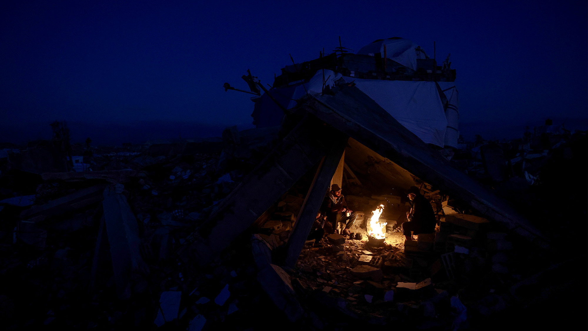 Displaced Palestinians warm up by the fire after their homes were destroyed in Gaza City, Palestine