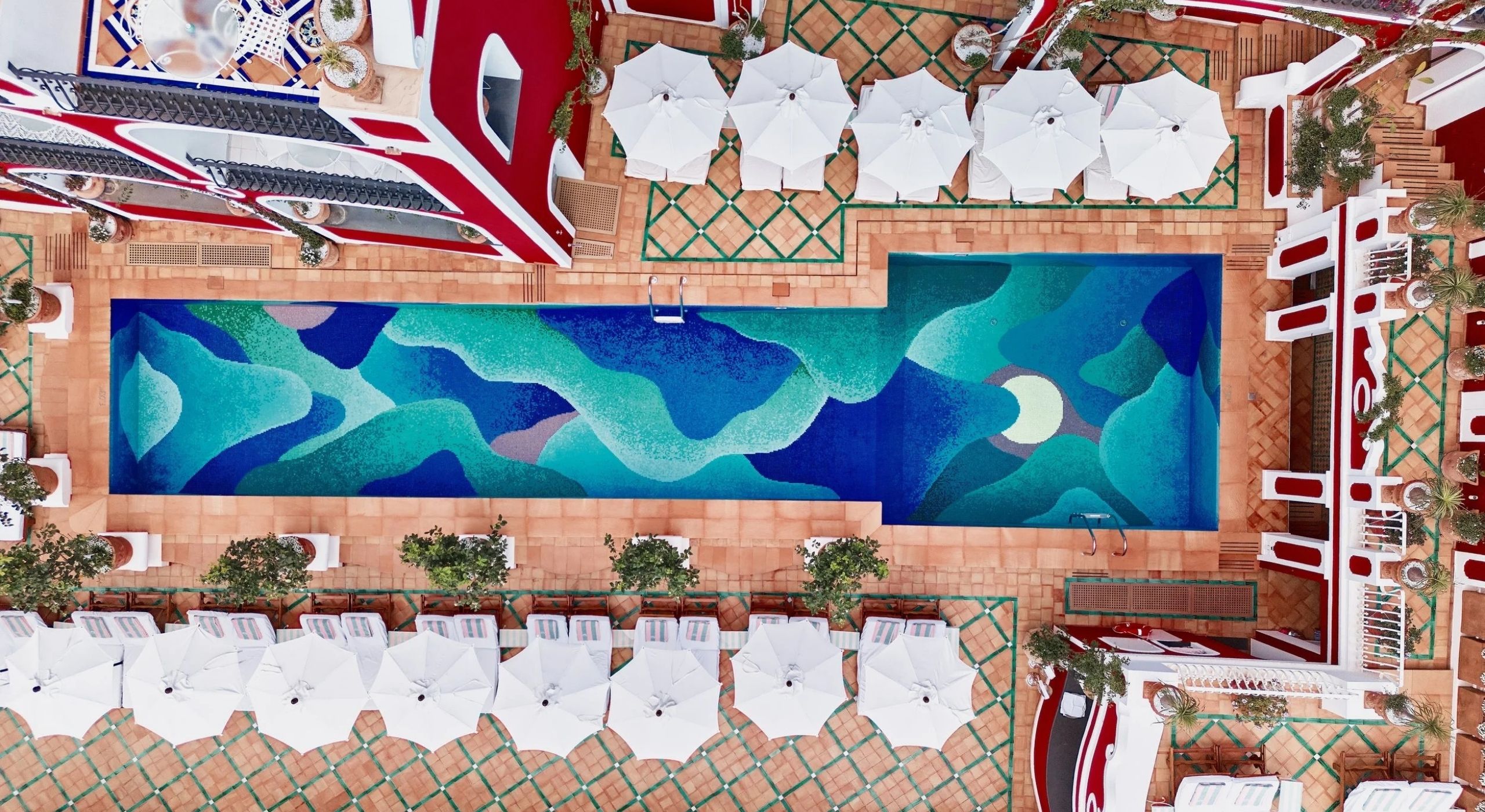 Aerial views of a colorful, vibrant pool with a bed made up of tiled waves in tones ranging from dark blue to green.