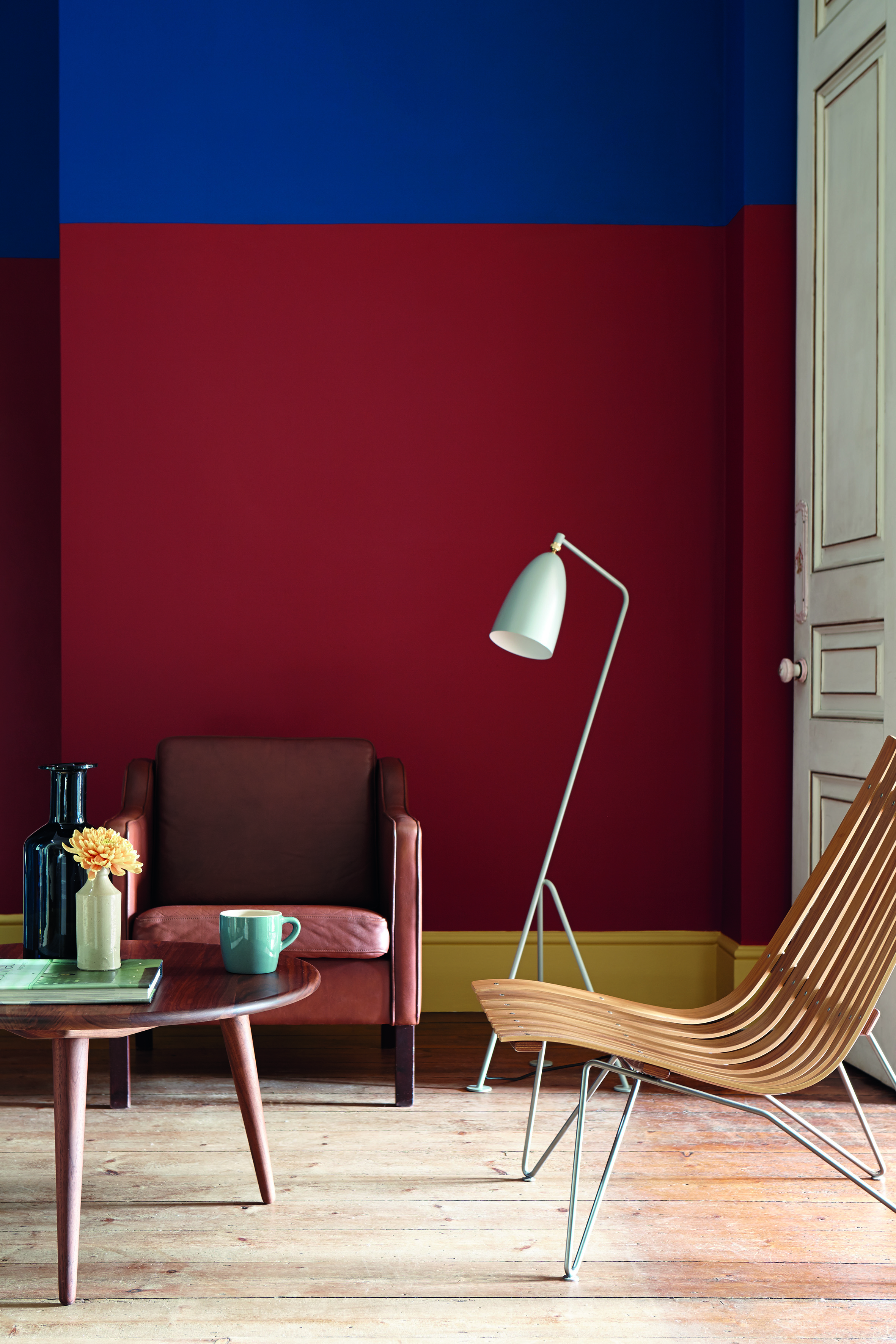 Red Living room with two armchairs and coffee table, floor lamp and wall painted in red and blue with yellow skirting board