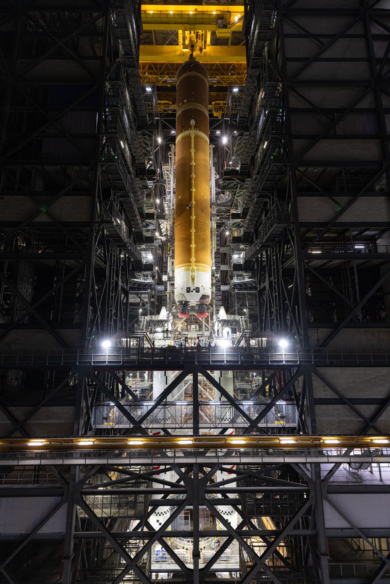 a large orange rocket booster is hoisted in a tall factory.